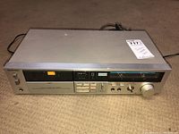 Front angle view of a Technics stereo cassette deck model M224 placed on a carpet floor. Shows the entire device including the buttons, dials, and cassette compartment.