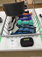 Photo showing all items in wire basket on table: the Harbinger belt, dumbbells, ankle/wrist weights, and mini boules case.