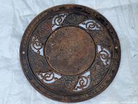 Full view of the round cast iron outer grate piece showing ornate scrollwork and flower motifs with an inscription on the outer rim