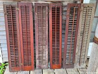 Six antique wooden indoor shutter panels arranged against a wall showing red/brown finish and aged metal hinges and hardware.