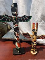 Two carved and painted wooden totem poles. One black painted about 12 inches tall, one smaller with natural wood color and bright paint.