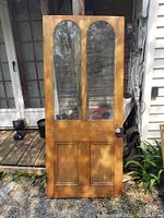 Full view of refurbished pine front door with two arched glass panes and old metal knobs.