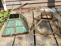 Two antique table lamp shades shown outside on wooden surface. One is a complete green stained glass shade with metal framing; the other is a matching metal frame shade without glass.
