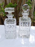 Pair of crystal decanters photographed outdoors on white cloth with foliage background.