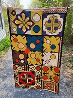 Full view of the large colorful woven wall hanging outdoors, showing overall pattern and colors.