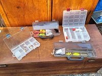 Four plastic tackle boxes laid open on a wooden surface showing a variety of fishing lures and accessories inside compartments.