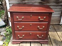Front view of the 3 drawer chest showing brass handles and keyholes, wood finish, and base details.