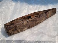 Rusty old cast iron axe or maul head, showing side angle with visible hole for handle and stamped marking.