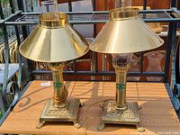 Pair of brass Orient Express reproduction electric lamps showing front and top angles with conical brass shades and bases with claw feet.