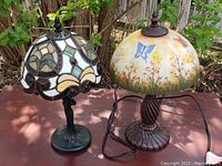 Pair of two small table lamps photographed outdoors on a wood surface, showing both lamps and their shades.