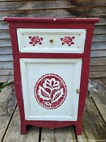 Front view of the small folk art cabinet with floral and rose decorations on door and drawer.