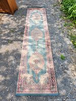 Full length view of the vintage runner rug laid out on ground showing turquoise medallion pattern and border.
