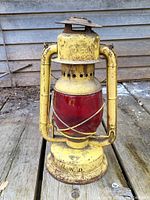 Vintage yellow metal lantern with red glass globe, showing front and side details, surface wear, and metal markings