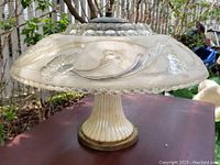 Side view of the glass light fixture on a table outdoors, showing floral and butterfly embossed glass shade and ribbed glass base.
