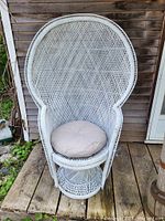 Front view of the vintage white wicker peacock chair placed outdoors with beige cushion on seat.