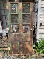 Full view of the vintage pine front door showing the top four glass panes, worn green and brown paint, metal hinges and the white knob on wooden backplate.