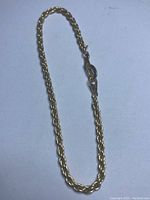 Full view of the gold plated rope chain bracelet and the lobster clasp on a plain background.
