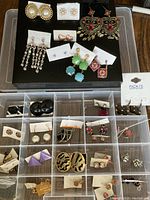 Top view of various earrings displayed on a black surface and compartments with multiple pairs ranked by style and color