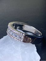 Front angled view of a polished sterling silver ring with three rows of small clear stones on top, resting on a translucent white crystal.