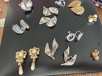 Top view of all 10 pairs of clip-on earrings arranged on a black surface showing various designs and styles.
