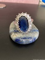 Front view of large blue gemstone ring showing oval faceted blue gem and clear stone halo.