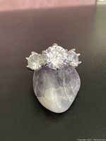 Front view of the sterling silver ring showing the large central clear gem and two smaller clear gems beside it, placed on a polished mineral stone