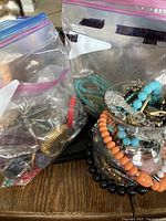 Photo of various bracelets and necklaces inside resealable plastic bags and a glass vase, showing colorful beaded and metallic jewelry.