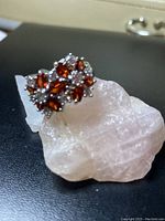 Close-up photo of red wine colored floral cluster ring placed on a translucent rock showing coordinated setting of stones and stamped silver band.