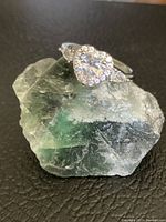 Close-up photo of the ring showing the large heart CZ center stone with side stones on a green textured base.