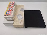 Three boxes and one black binder closed and stacked for size reference.