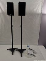 Both Precision Acoustics HD4 bookshelf speakers mounted on Perlesmith adjustable black speaker stands, additional hardware and a water bottle for scale.