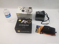 Photo of Nikon Coolpix L16 and 4800 camera boxes, Polaroid Impulse camera with strap, Lowepro Rezo 30 camera bag, and water bottle for scale.