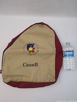 Front side of backpack showing tan panel with 2002 World Youth Day Toronto logo and Canada branding, next to water bottle for scale.