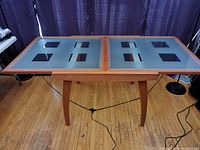 Front view of the Italian dining table showing the frosted glass top with clear glass square insets and wooden frame and legs.