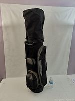 Black golf bag standing upright with multiple pockets visible, with a water bottle for scale.