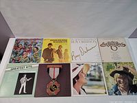 Photo of 8 vinyl records laid out in 2 rows, showing front covers including The Guess Who, Mamas and Papas, Roy Orbison, The Oak Ridge Boys, and others.