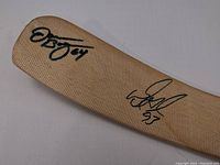 Close-up image of the beige blade of the wooden hockey stick with two signatures in black marker, Doug Gilmour's signature includes the number 93, the second signature includes the number 45.