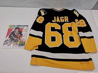 Back view of black CCM hockey jersey with number 68 and name Jagr, alongside bagged Beckett Magazine featuring hockey cover.