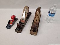 Three hand planes of varying sizes from Stanley, Prestige and Craftsman beside a water bottle for scale.
