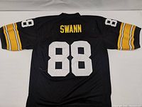 Back of a black Pittsburgh Steelers football jersey showing stitched yellow name 'SWANN' and large white number '88'. Sleeves have yellow and white stripes.