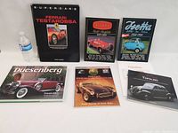 Six car books arranged on table. Books include Ferrari Testarossa Supercars, Duesenberg, Allard Gold Portfolio, Isetta BMW-Iso-Velam, and two Topolino books. Water bottle for scale.