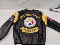 Back of black leather jacket showing large Pittsburgh Steelers logo with yellow and white stripes on sleeves.