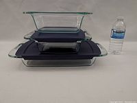 Side view of three stacked clear Pyrex glass containers with two black lids between them, and a water bottle for scale.