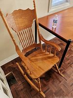 Full view of wooden rocking chair showing seat, armrests, turned spindles, and rockers.