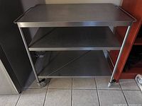 Full front view of stainless steel kitchen cart showing three shelves and wheels.