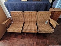 Front view of the three connected wicker seats with armrests on two sides and metal frame base.