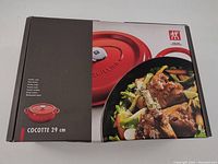 Front view of the boxed Zwilling J.A. Henckels 29cm oval cocotte/dutch oven in red, showing product photos and branding.