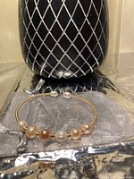 Front view of the bangle displayed on a silver satin pouch with a black and white patterned vase in the background.