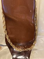 Photo of the necklace displayed on a brown stand showing the twisted rope design and bright gold tone.