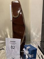 Bright 18k gold electroplated necklace draped over brown display stand, standing upright, with auction lot number 82 shown and a blue gift box nearby.